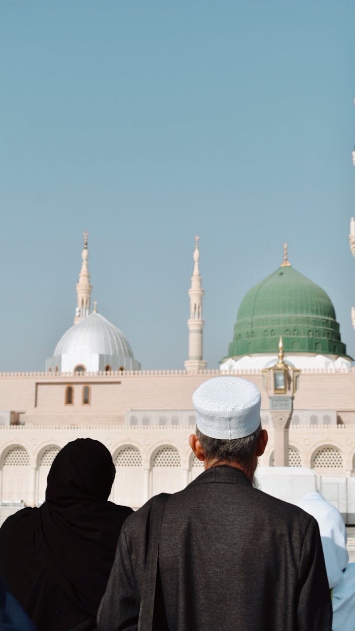 Two pilgrims facing Al-Masjid an-Nabawi's iconic green dome in Medina.